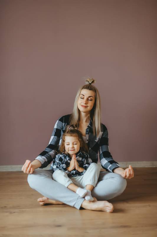 Young woman sitting on the floor in a living room with her little daughter in a lotus pose with closed eyes Motherhood, happy lifestyle concept. Vertical portrait